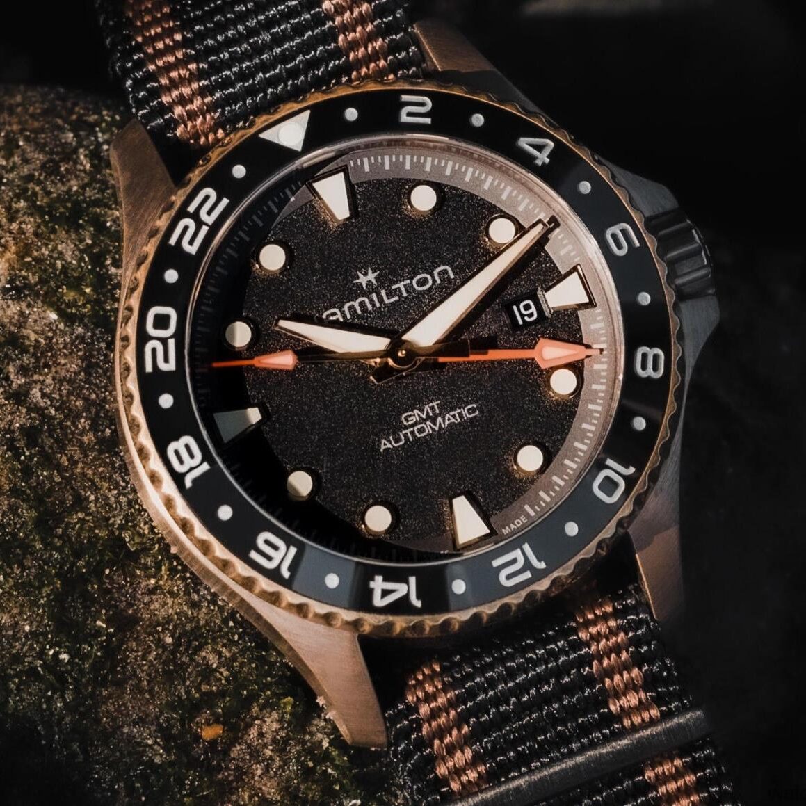 Hamilton wristwatch with a black and gray NATO strap on a textured surface.