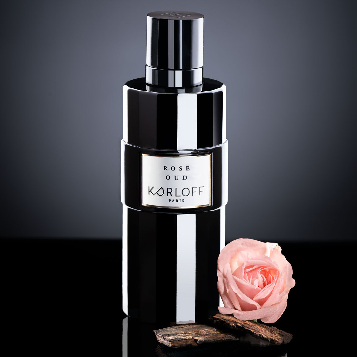Elegant black perfume bottle with a soft pink rose beside it.