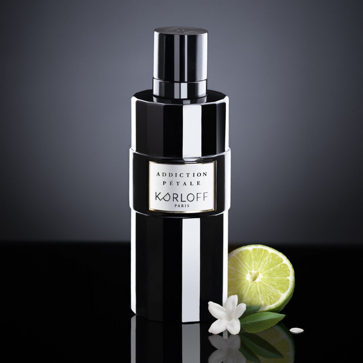 Elegant black perfume bottle with a lime and white flower beside it.